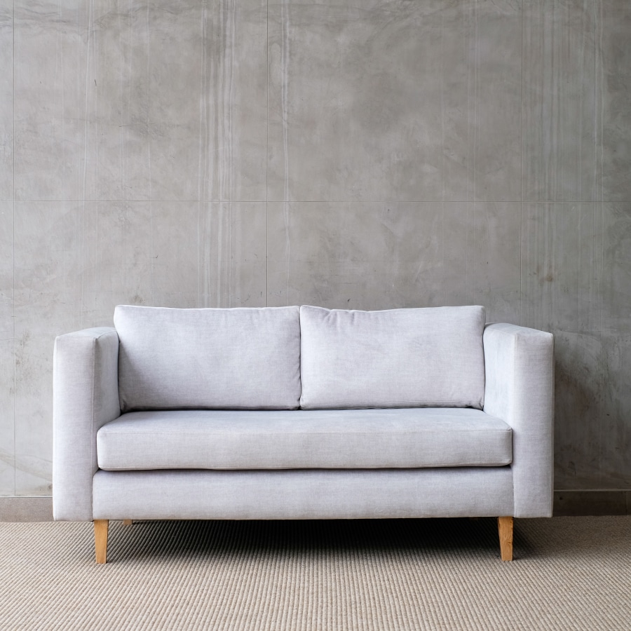 Single Greay Couch with wooden legs against a grey wall